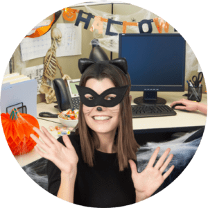 A woman in a cat costume is in a Halloween-themed office with decorations and a skeleton.
