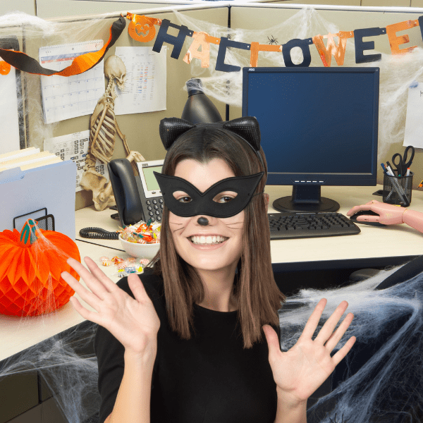 A woman in a cat costume is in a Halloween-themed office with decorations and a skeleton.