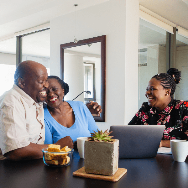 A happy group of people sitting together at a table with a laptop and food, smiling and enjoying each other's company.