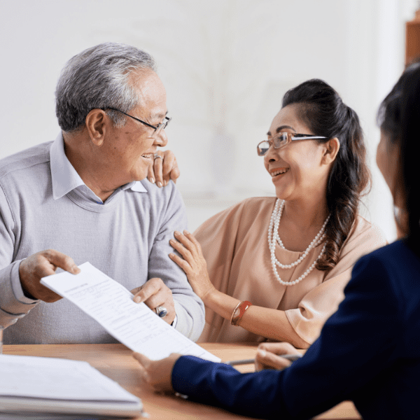 An elderly couple is smiling while discussing documents with another person, possibly related to planned giving.
