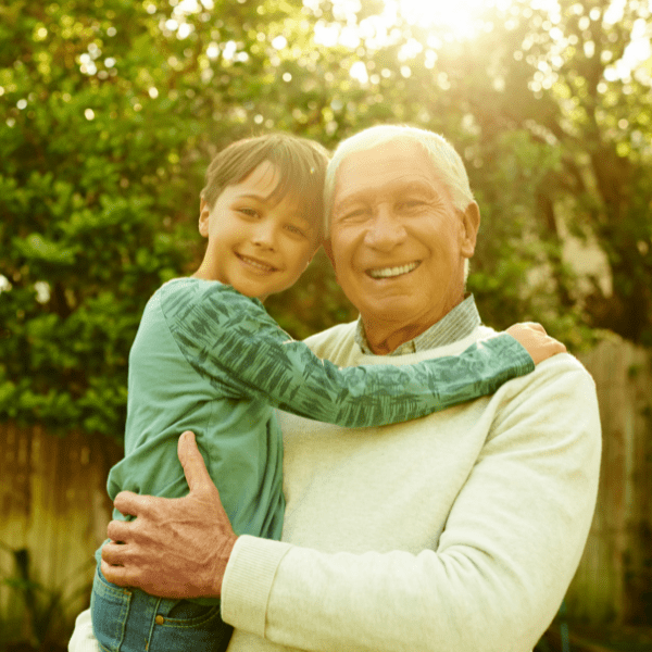 An older man and a child are smiling and embracing outdoors.
