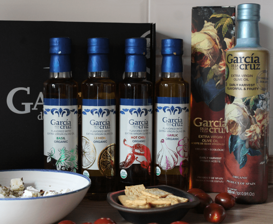Bottles of flavored extra virgin olive oils with a bowl of cheese, a plate of crackers, and cherry tomatoes.