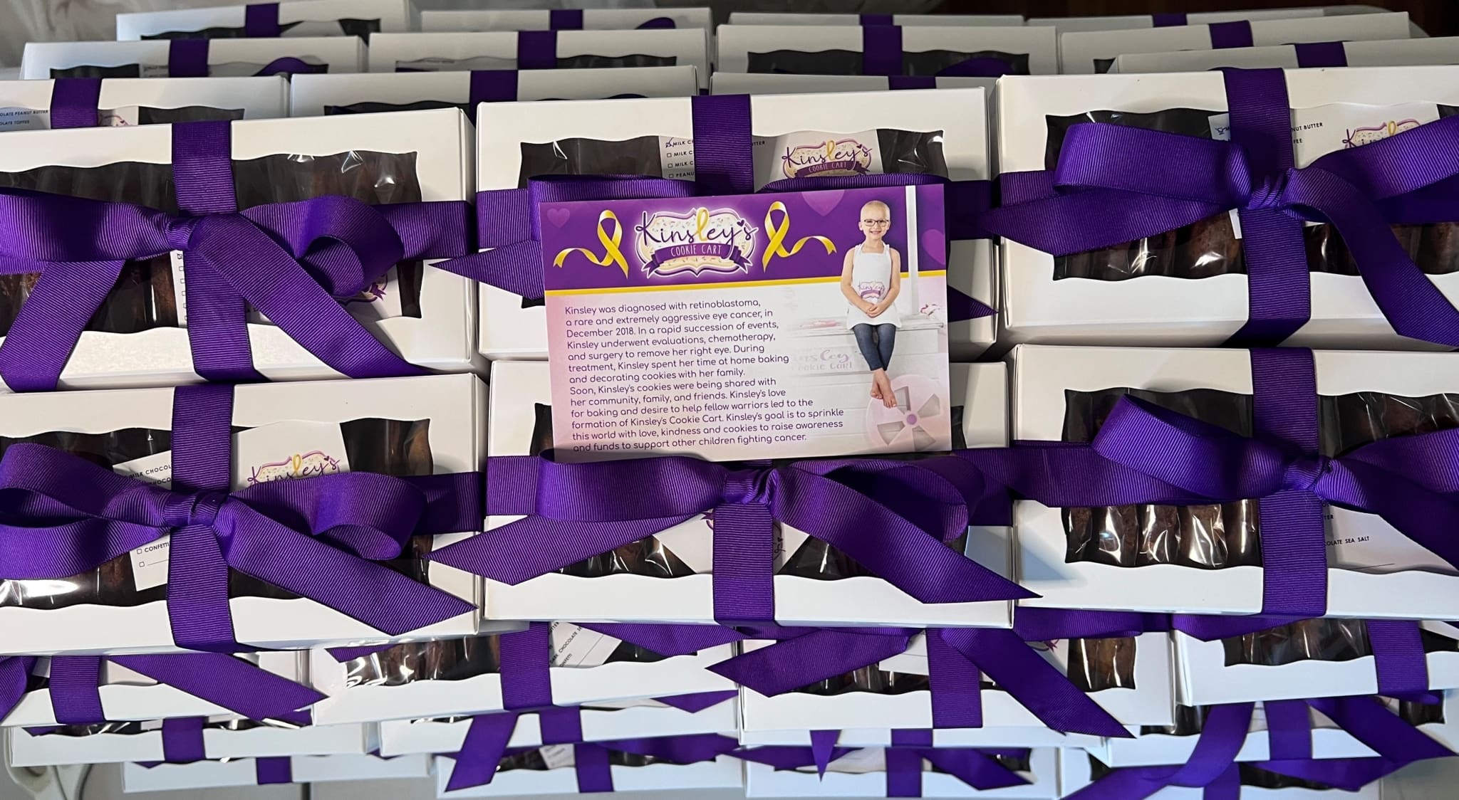 Boxes of cookies tied with purple ribbons, supporting a cause to raise awareness and funds for children fighting cancer. Gifts that give back.